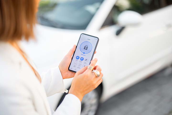 Woman closes the door or turns on the car alarm with a mobile phone. Device with running program for vehicle security. Innovative technologies in car security and access