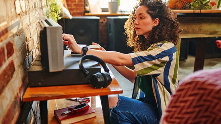 What Does a True Audiophile Need at Home? Building the Ultimate Sound Sanctuary; Modern young woman in stylish casualwear turning amplifier on portable radio receiver while regulating volume or switching new station