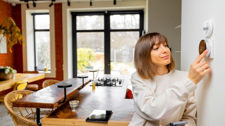 Woman adjusting smart thermostat temperature in modern kitchen